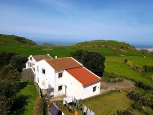 een wit huis met een rood dak op een groen veld bij Casa da Mediana in Ribeira Grande