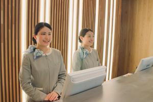 une femme debout à une table devant un miroir dans l'établissement Richmond Hotel Matsumoto, à Matsumoto