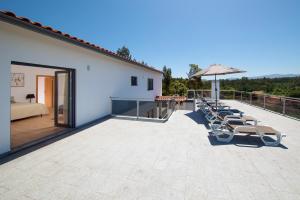 une grande terrasse avec des chaises longues et un parasol dans l'établissement Casa Bem Estar, à Vila Nova de Poiares