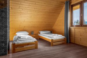 two beds in a room with wooden walls and windows at Miodówka - komfortowy dom w górach in Glinka