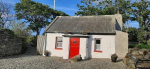 a small white house with a red door at Cherry Tree Cottage - Cosy 19th Century Cottage in Claragh