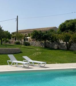 - deux chaises longues blanches installées à côté de la piscine dans l'établissement Casale Zacco Micciò, à Rosolini