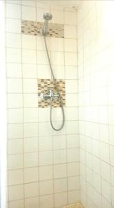 prysznic z wężem w wyłożonej białymi kafelkami łazience w obiekcie le Refuge d'Eugénie w mieście Bahus-Soubiran