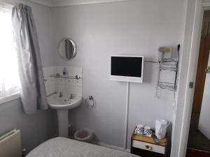 baño blanco con lavabo y TV en la pared en Seashells Guest House, en Great Yarmouth