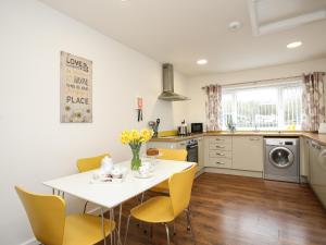 a kitchen with a white table and yellow chairs at Bwthyn Tyn y Coed in Bryngwran