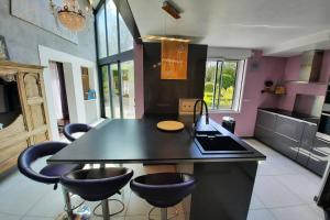 a kitchen with a black island with bar stools at Maison Jeanne (proche Bécherel pour 14 personnes) in Saint-Pern