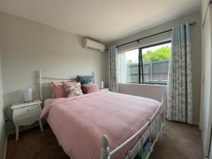 a bedroom with a bed with pink sheets and a window at Auckland Cornwall Park holiday Home in Auckland