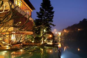 a building with a tree next to a river at night at Volando Urai Spring Spa & Resort in Wulai