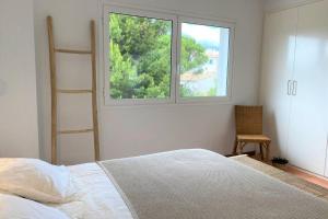 um quarto com uma cama, uma janela e uma cadeira em LLEBEIG -Casa mediterránea con gran jardín em Cadaqués