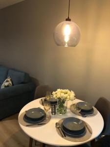a white table with plates and glasses and a light at Apartament Kameleon in Dźwirzyno