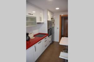 a kitchen with white cabinets and a red counter top at Dúplex con soleada terraza! in Renedo de Piélagos