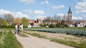 two people walking down a dirt road next to a field at Vakantiehuis Ooglée in Hooglede