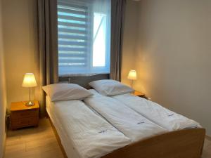 Bett mit weißer Bettwäsche und Kissen in einem Zimmer mit Fenster in der Unterkunft Wolin-Travel Apartament Park in Misdroy