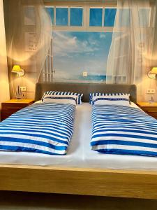 twee bedden met blauwe en witte gestreepte kussens voor een raam bij Ferienresidenz Seegarten -Andrea App1 - beheizter Indoor-Pool in Bodman-Ludwigshafen