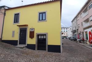 a yellow building with black doors on a street at Taska Vila Velha in Mirandela
