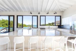 a kitchen with a large island with white chairs at Sandcastle Beach House in The Valley