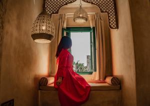 Una donna con un vestito rosso che guarda fuori da una finestra di DECAN Concept Boutique Estate a Città di Rodi