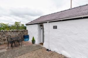 a white cottage with a table and chairs on a patio at Eithin Bach in Caernarfon