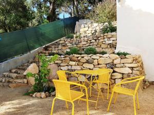 Villa_Culomba ALATA -T2 4 couchages في Alata: طاولة وكراسي صفراء أمام جدار حجري