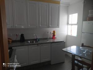 cocina con armarios blancos, fregadero y mesa en Apartamento Manuel, en Vilagarcía de Arousa