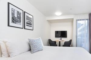 a white bedroom with a bed and a tv at City Edge North Melbourne Apartment Hotel in Melbourne