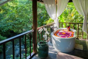 eine Badewanne auf dem Balkon mit Blick auf die Bäume in der Unterkunft Komaneka at Bisma Ubud in Ubud