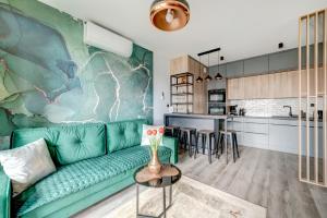 a living room with a green couch and a kitchen at Live & Travel Apartments Grano Residence in Gdańsk