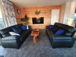 a living room with two leather couches and a tv at Folia Domus NZ, Redwoods, MBT in Rotorua