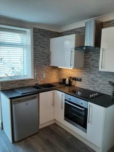 a kitchen with white cabinets and black counter tops at Beachmount Holiday Apartments in Colwyn Bay
