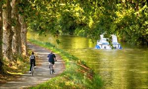 two people riding bikes down a path next to a river at L'atelier in Capestang