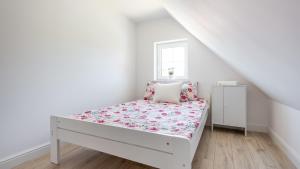 a white bedroom with a bed with a floral bedspread at Domek Magda in Gdańsk
