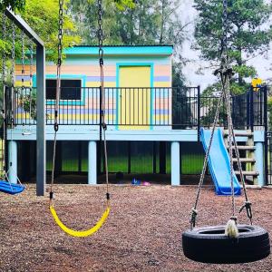 a playground with three swings in front of a building at Mountainview Escape Rothbury 5br house in Rothbury