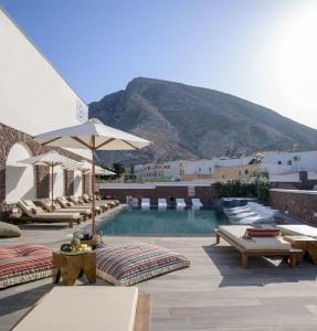 a pool with chairs and an umbrella and a mountain at Selini Ηotel in Kamari
