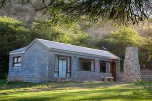 une petite maison en pierre sur une pelouse dans l'établissement Baviaanskloof Guest Cottages, à Studtis
