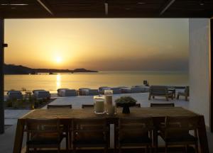 a dining table with chairs and a sunset in the background at Domes White Coast Milos, Adults Only - Small Luxury Hotels of the World in Mytakas