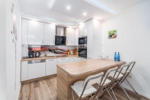 a kitchen with white cabinets and a wooden table and chairs at Seaside Breeze Stylish Apartment Balcony & Parking by Renters in Międzyzdroje