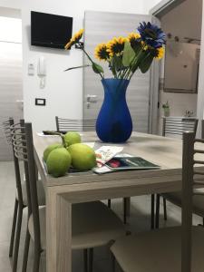 a table with a blue vase with flowers and fruit on it at Casa Àbola in Avola