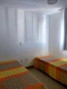 deux lits dans une chambre avec des murs et des fenêtres blancs dans l'établissement Edifício Gil Nogueira, apartamento aconchegantes, piscina, sauna, Wiff, duas vagas de garagem., à Guarapari