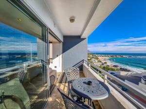 Clifton YOLO Spaces - Clifton Beachfront Executive Apartment في كيب تاون: شرفة مع طاولة وكراسي والمحيط