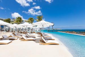 a pool with chairs and umbrellas and the ocean at The Morgan Resort Spa & Village in Simpson Bay