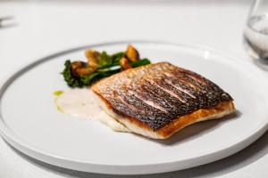 a white plate with a piece of fish and vegetables at Hyatt Regency Malta in St. Julianʼs