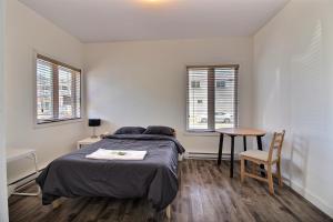 a bedroom with a bed and a table and two windows at Chambres en ville La Tuque in La Tuque