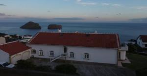 a white house with a red roof next to the ocean at Ocean Front View in Angra do Heroísmo