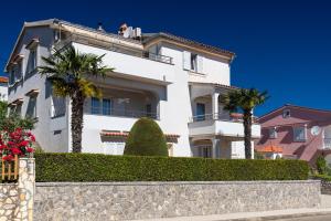 a white house with palm trees in front of it at Apartments Stipančić in Krk