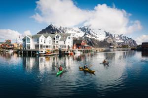 three people in kayaks on a body of water with mountains at Villa Bryggekanten - by Classic Norway Hotels in Henningsvær