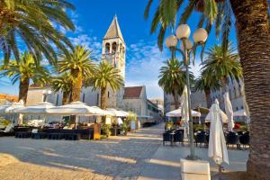a street with palm trees and a church with a clock tower at Apartment in Trogir with sea view, terrace, air conditioning, Wi-Fi (3788-2) in Trogir