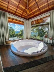 a large bath tub in a room with large windows at Refúgio Physis Suítes in Monte Verde