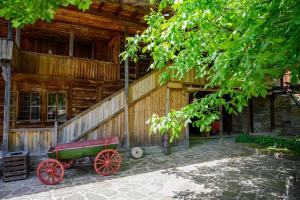 um edifício de madeira com uma carroça vermelha à sua frente em Guest Houses "Zlatna Oresha - Complex" em Zheravna
