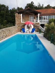 una piscina con 2 sillas y una sombrilla roja en A Quinta da Colina ( Casinha ) en Castanheira de Pêra