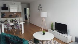 a living room with a white table and a kitchen at Apartament Szmaragdowy Zakątek in Kołobrzeg